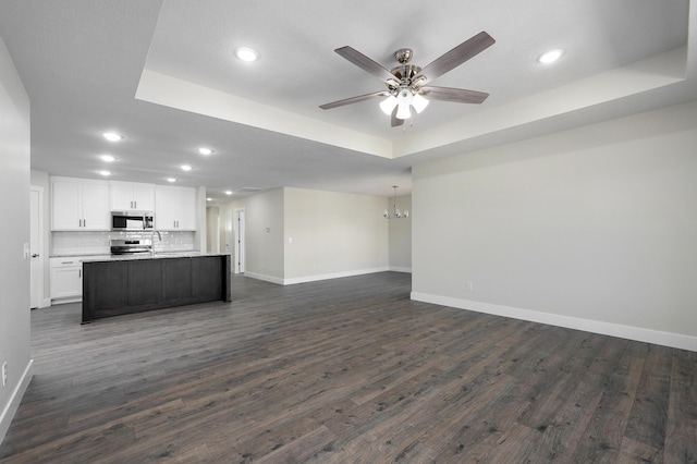 unfurnished living room featuring dark wood-type flooring, ceiling fan, a raised ceiling, and sink