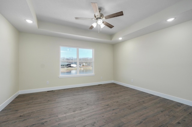 spare room featuring dark wood-type flooring, ceiling fan, and a tray ceiling