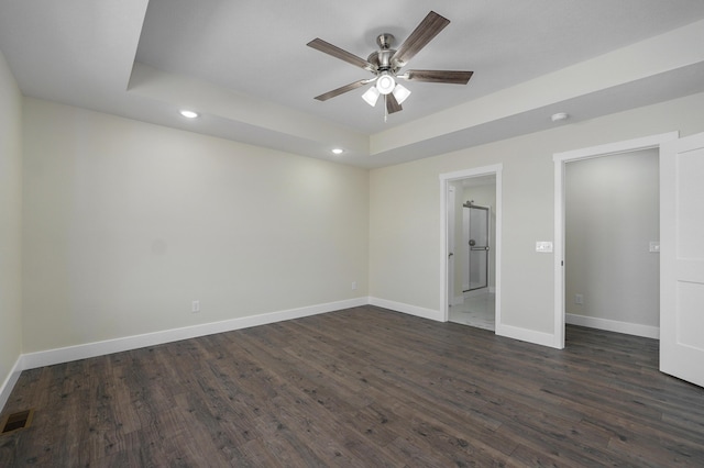 unfurnished bedroom with dark wood-type flooring, ceiling fan, ensuite bathroom, and a tray ceiling