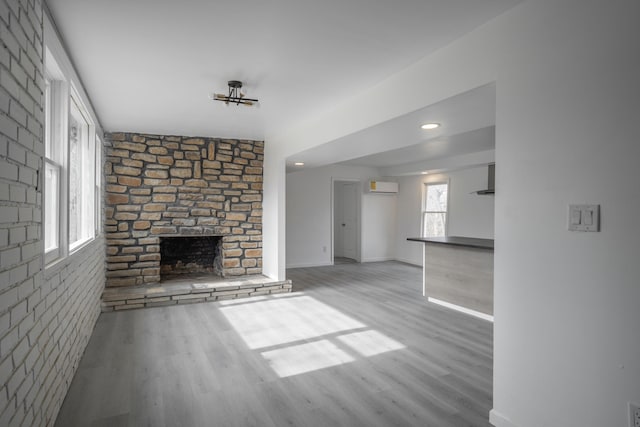 unfurnished living room with an AC wall unit, a large fireplace, and light wood-type flooring