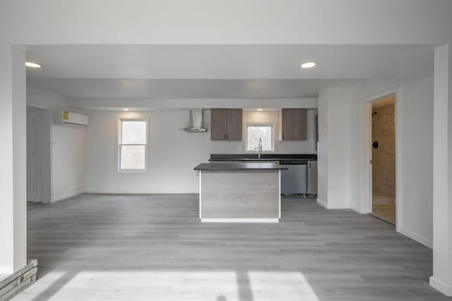 kitchen featuring a wall unit AC, dishwasher, light hardwood / wood-style floors, and wall chimney exhaust hood