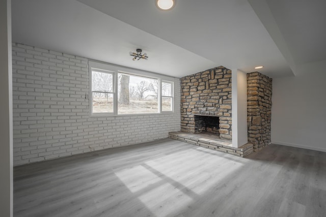 unfurnished living room featuring a fireplace, wood-type flooring, and brick wall