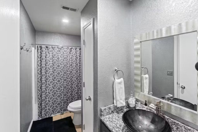 bathroom featuring walk in shower, vanity, toilet, and tile patterned flooring