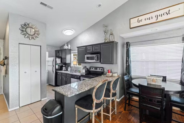 kitchen featuring light tile patterned flooring, lofted ceiling, kitchen peninsula, stainless steel appliances, and light stone countertops