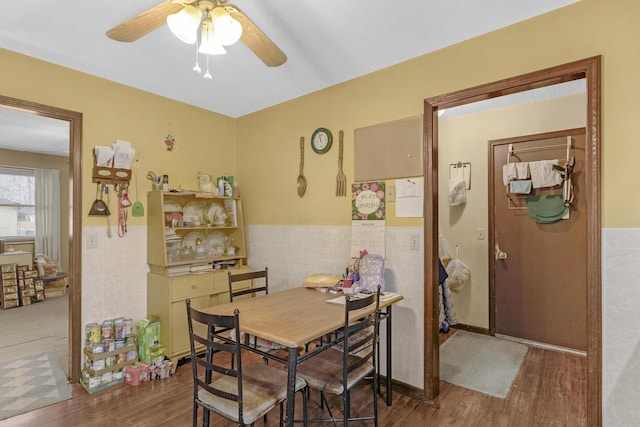 dining area featuring ceiling fan, wood-type flooring, and tile walls