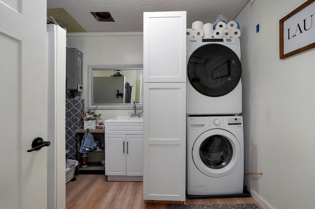 laundry room with stacked washing maching and dryer, sink, cabinets, light hardwood / wood-style floors, and a textured ceiling