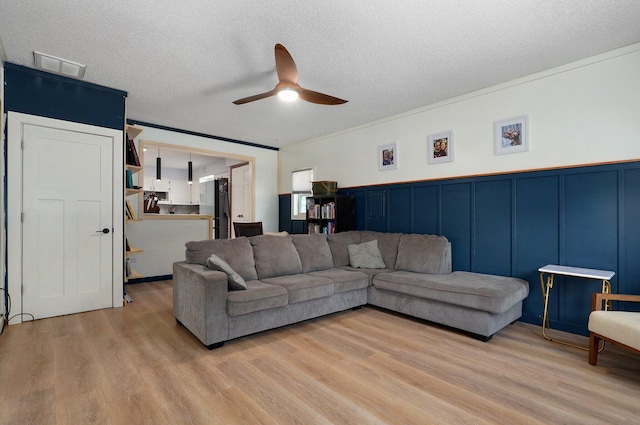 living room featuring ceiling fan, crown molding, light hardwood / wood-style flooring, and a textured ceiling