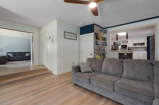 living room featuring ceiling fan, a textured ceiling, and light wood-type flooring