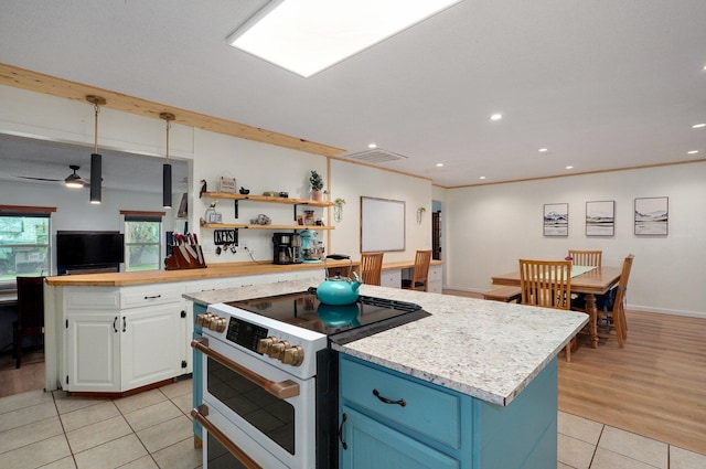 kitchen with decorative light fixtures, high end white range, white cabinets, a center island, and light tile patterned floors