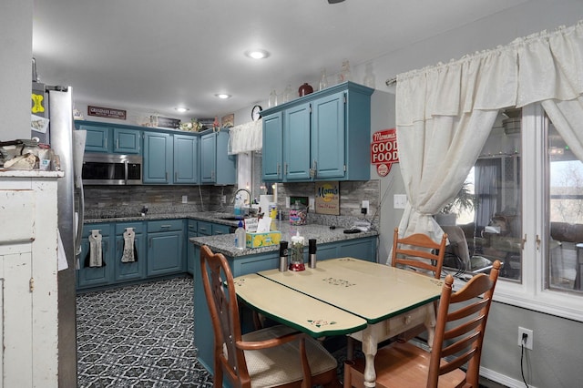 kitchen with sink, dark stone countertops, backsplash, stainless steel appliances, and blue cabinets