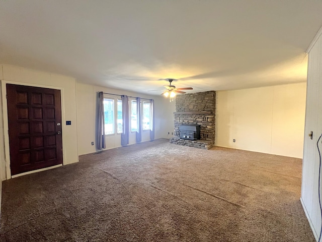 unfurnished living room featuring ceiling fan, a stone fireplace, and carpet floors