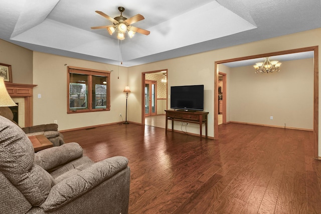 living room featuring dark hardwood / wood-style floors, ceiling fan with notable chandelier, and a tray ceiling