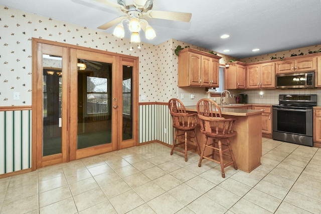 kitchen featuring sink, light tile patterned floors, a breakfast bar, appliances with stainless steel finishes, and kitchen peninsula