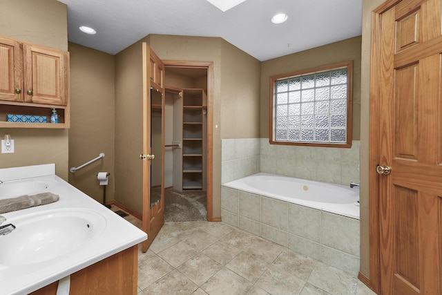 bathroom with a relaxing tiled tub, vanity, and tile patterned floors