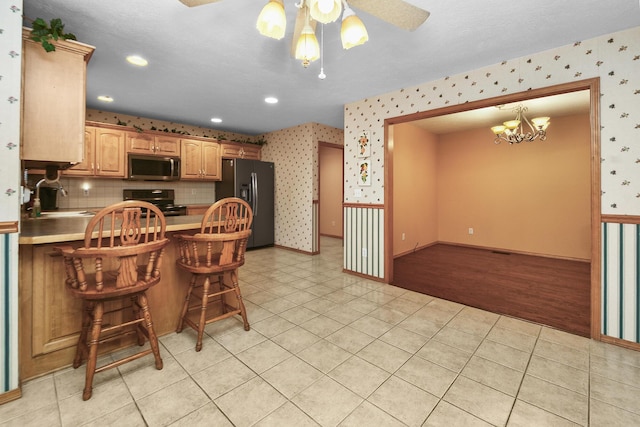 kitchen featuring a breakfast bar, sink, black fridge, hanging light fixtures, and range with electric cooktop