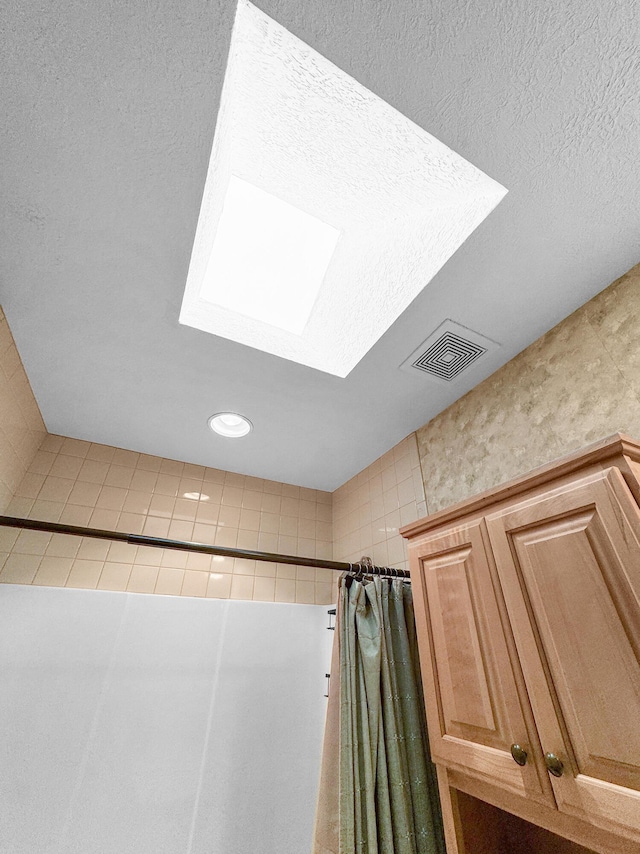 room details with walk in shower, a skylight, and a textured ceiling