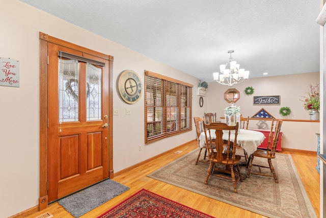 dining space with a textured ceiling, an inviting chandelier, and light hardwood / wood-style flooring