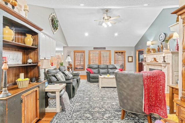 living room featuring a tile fireplace, vaulted ceiling, ceiling fan, and light wood-type flooring