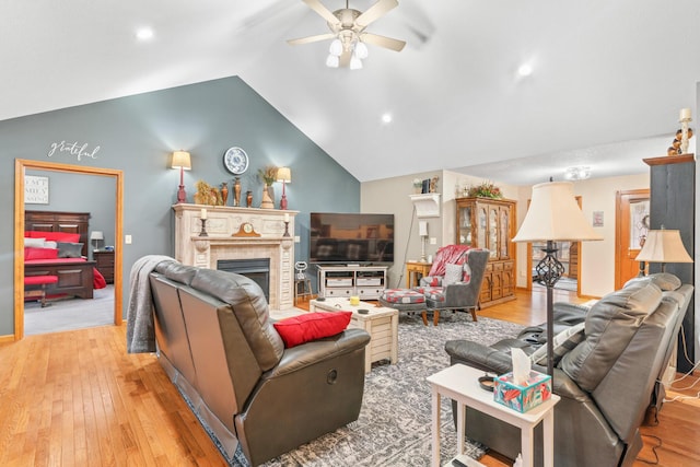 living room with a tiled fireplace, ceiling fan, lofted ceiling, and light hardwood / wood-style floors