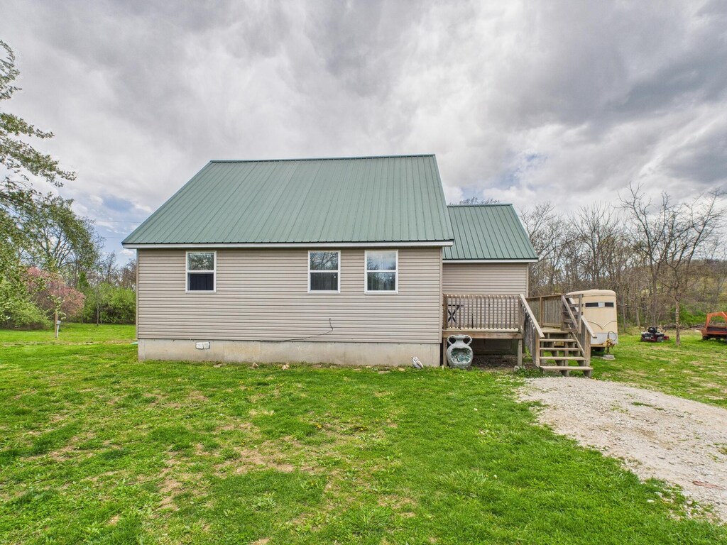 back of house with metal roof, a wooden deck, and a lawn