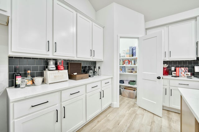 kitchen with white cabinetry, light countertops, light wood-style flooring, and tasteful backsplash