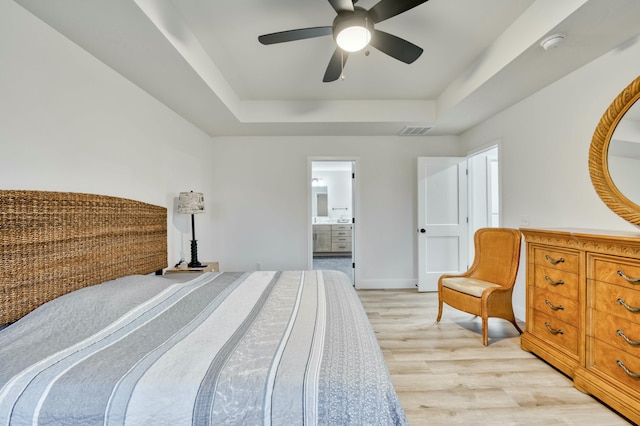 bedroom with light wood-type flooring, visible vents, a tray ceiling, baseboards, and ceiling fan