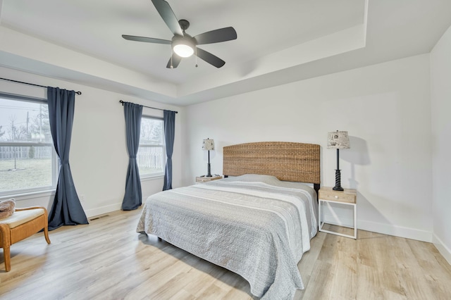 bedroom featuring visible vents, baseboards, a tray ceiling, and wood finished floors