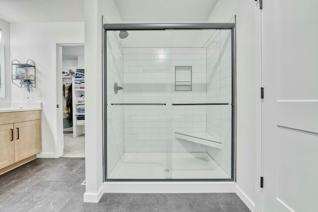 bathroom featuring a spacious closet, a shower stall, vanity, and baseboards