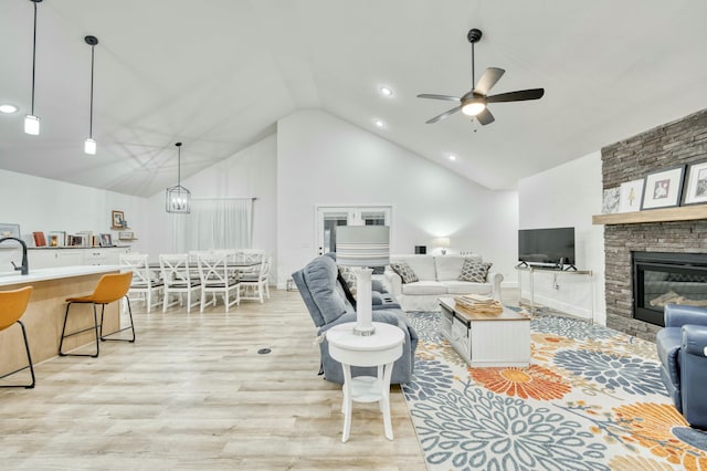 living area featuring light wood-type flooring, high vaulted ceiling, a stone fireplace, and ceiling fan