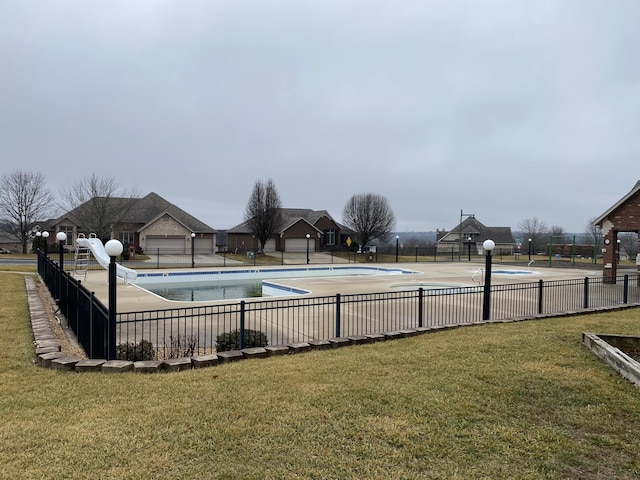 community pool with a yard, fence, and a water slide