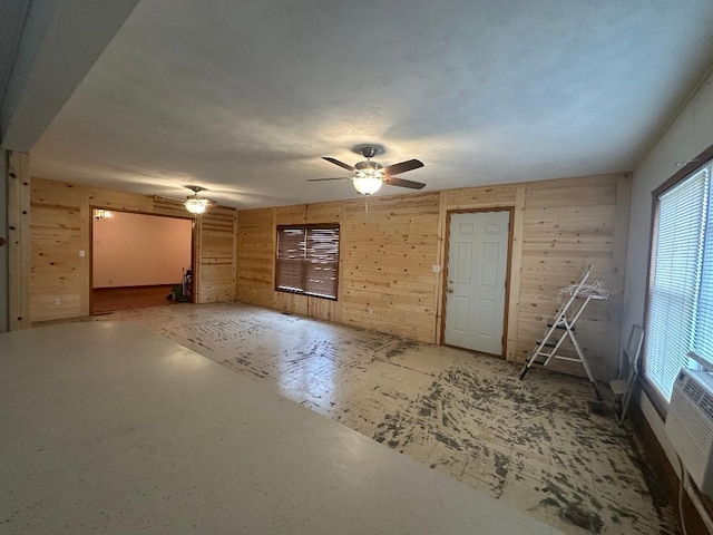 unfurnished living room featuring ceiling fan and wooden walls