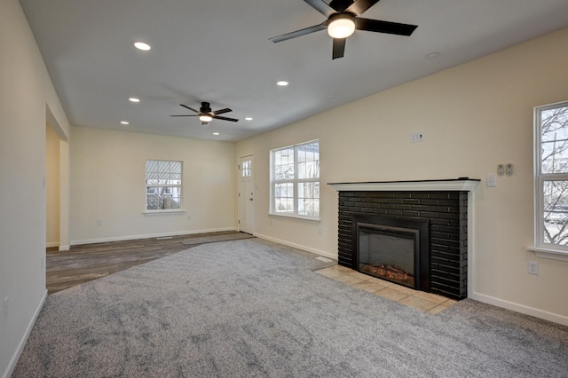 unfurnished living room featuring ceiling fan, a fireplace, and light carpet