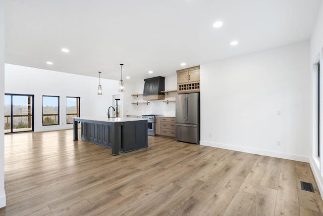 kitchen with sink, premium appliances, a kitchen island with sink, pendant lighting, and light hardwood / wood-style floors