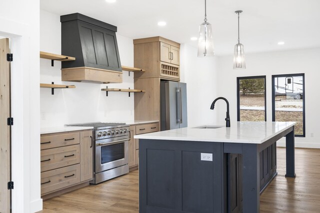 kitchen featuring sink, premium appliances, custom range hood, a center island with sink, and decorative light fixtures