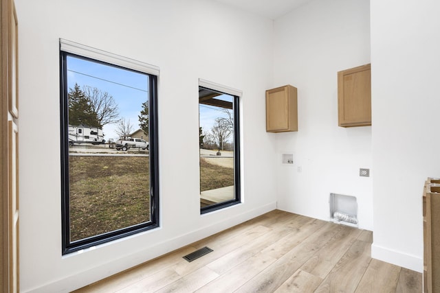 laundry room with washer hookup, electric dryer hookup, light hardwood / wood-style floors, and cabinets