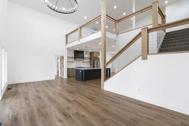 unfurnished living room with a high ceiling, dark wood-type flooring, sink, and a chandelier