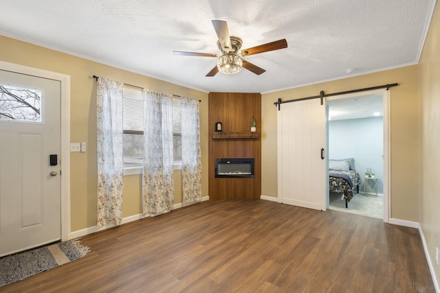 unfurnished living room with dark hardwood / wood-style flooring, ornamental molding, a barn door, and ceiling fan