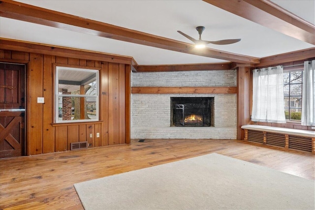 unfurnished living room with beamed ceiling, wood-type flooring, a brick fireplace, and wooden walls