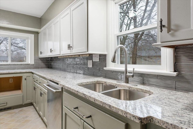 kitchen with a wealth of natural light, dishwasher, sink, backsplash, and light stone countertops