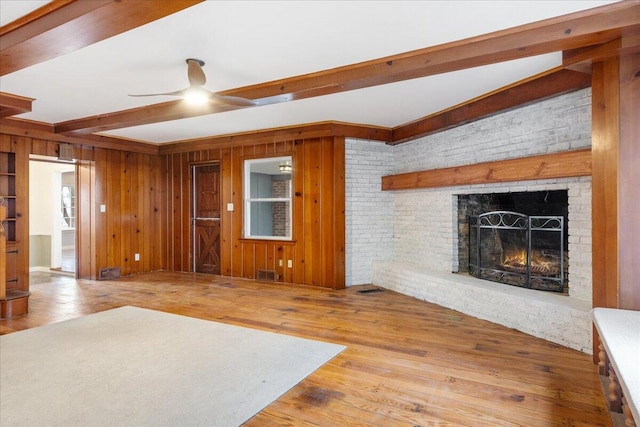 unfurnished living room featuring beamed ceiling, wood-type flooring, wooden walls, and a brick fireplace