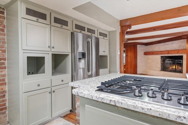 kitchen featuring a brick fireplace, stainless steel appliances, beamed ceiling, and brick wall