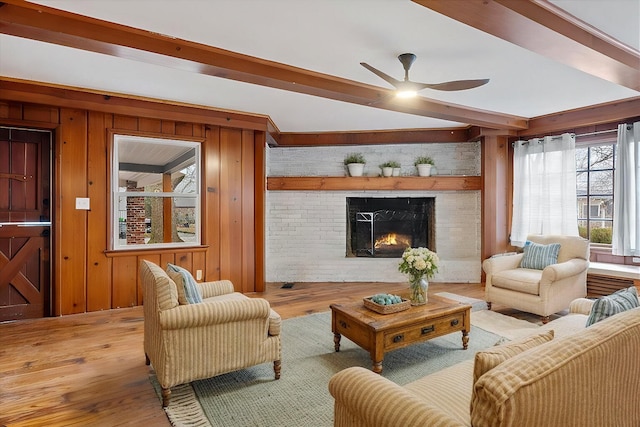 living room featuring a brick fireplace, light hardwood / wood-style floors, beamed ceiling, and wood walls