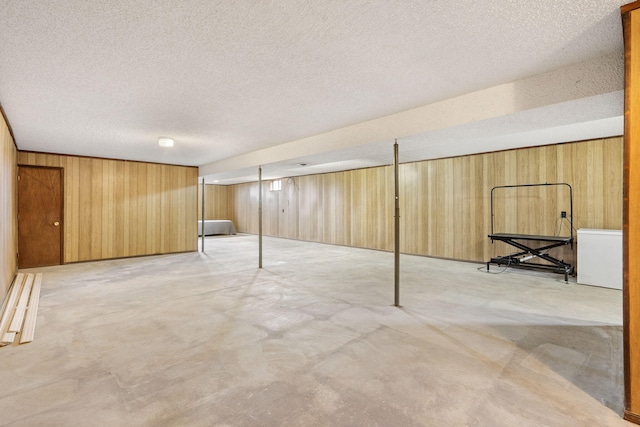 basement featuring refrigerator, a textured ceiling, and wood walls