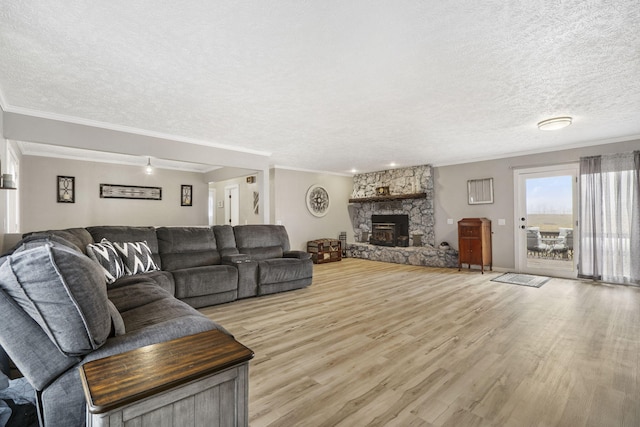 living room featuring a stone fireplace, light hardwood / wood-style flooring, ornamental molding, and a textured ceiling