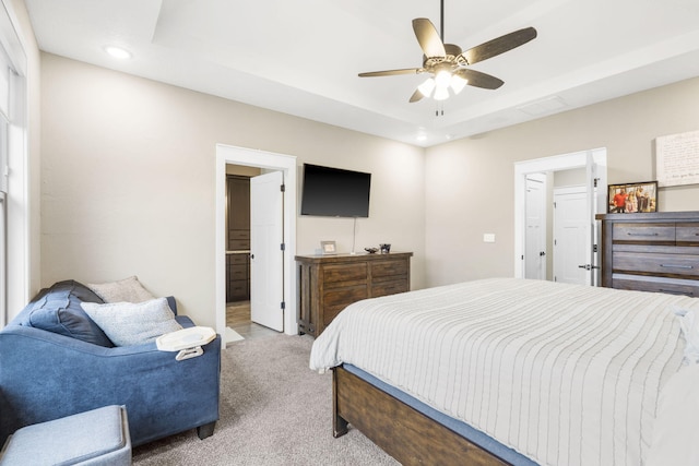 carpeted bedroom featuring a raised ceiling, ensuite bathroom, and ceiling fan