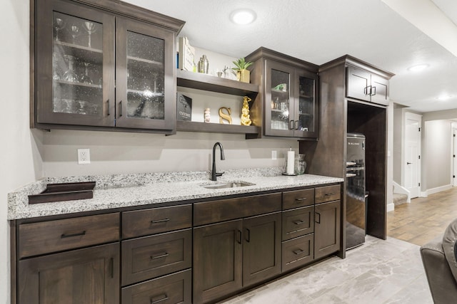 kitchen featuring light stone countertops, dark brown cabinets, and sink