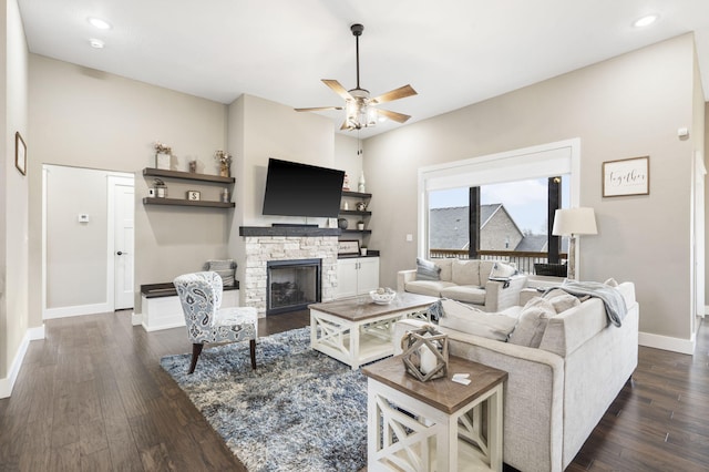 living room featuring dark hardwood / wood-style flooring, a stone fireplace, and ceiling fan