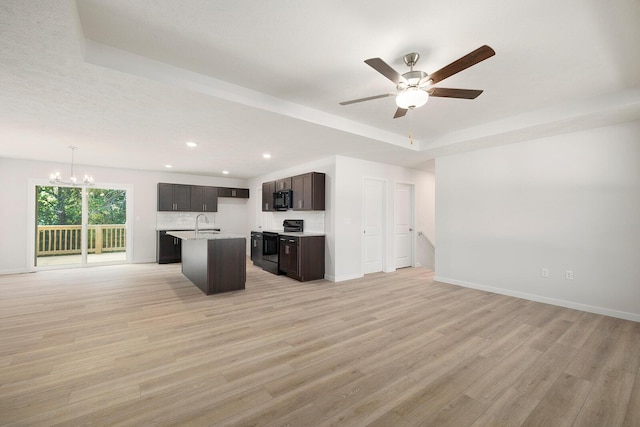 kitchen with electric stove, light hardwood / wood-style floors, a center island with sink, decorative light fixtures, and a raised ceiling