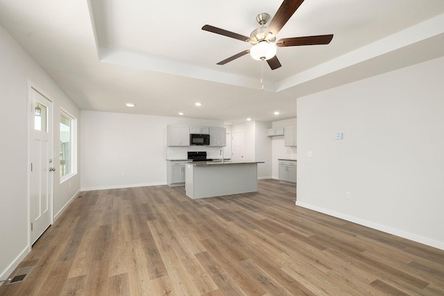 unfurnished living room with ceiling fan, a raised ceiling, and light hardwood / wood-style flooring