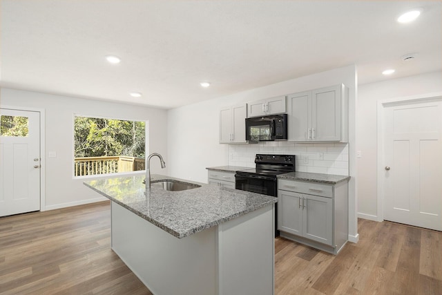 kitchen with a kitchen island with sink, sink, black appliances, and light stone countertops